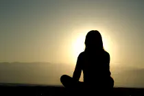 The silhouette of a woman sitting cross-legged in front of a setting sun