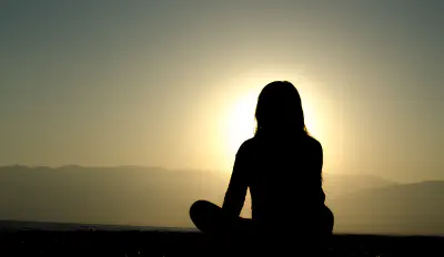 The silhouette of a woman sitting cross-legged in front of a setting sun
