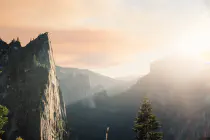 The sun shining brightly over a verdant valley with steep cliff faces