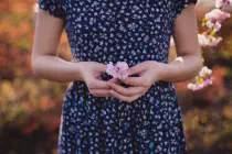 A woman in a blue patterned dress holding a small pink flower