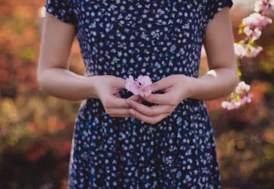 A woman in a blue patterned dress holding a small pink flower