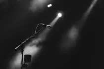 A black and white photo of a microphone on a stage with dramatic spot lighting