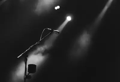 A black and white photo of a microphone on a stage with dramatic spot lighting